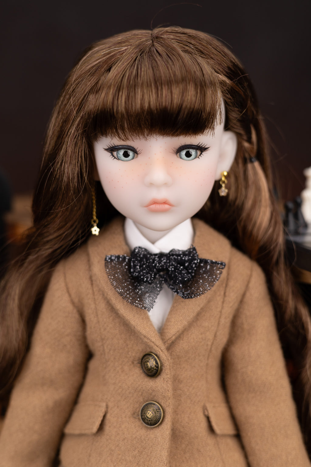 Doll wearing a brown coat with a black bow tie against a dark background