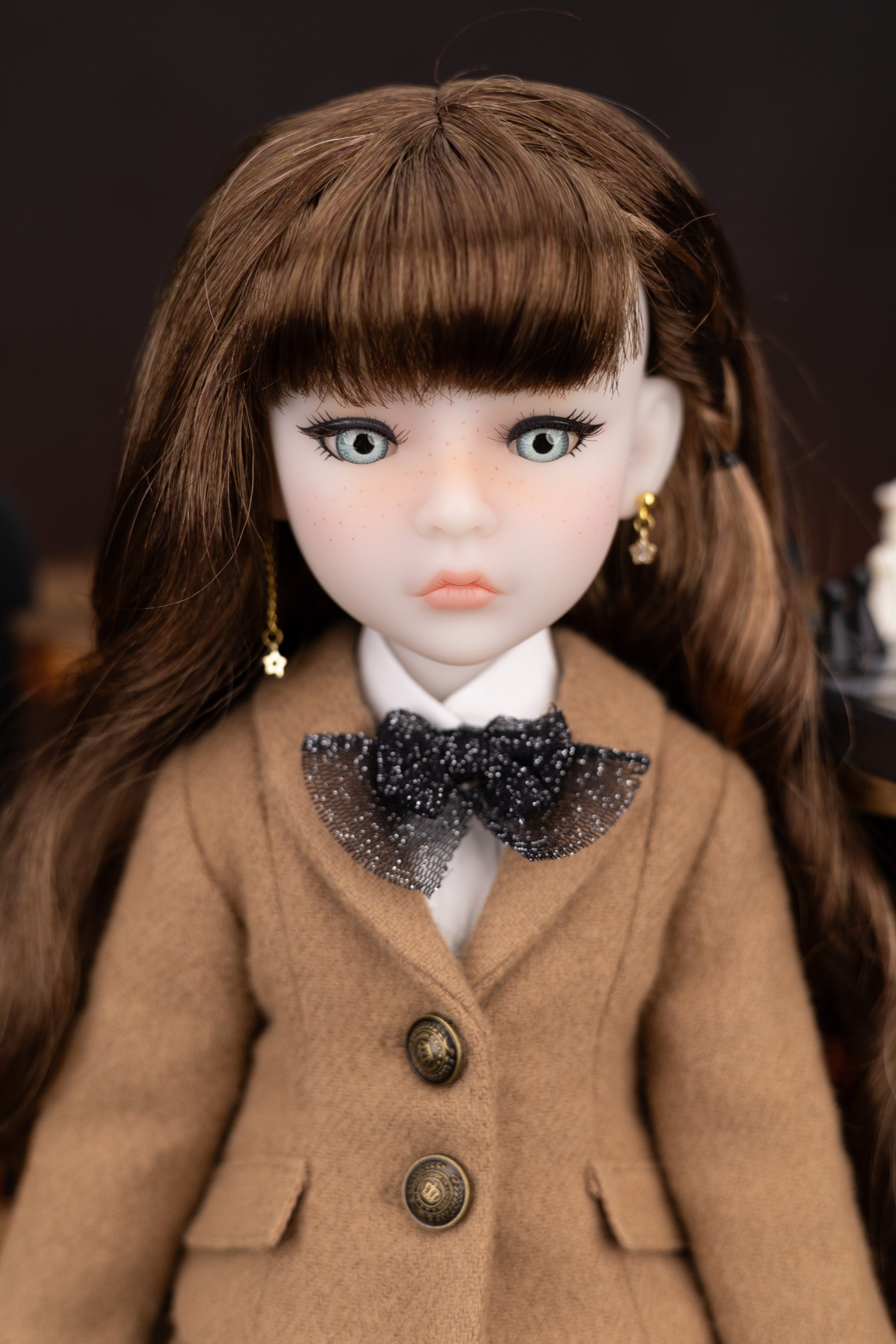 Doll wearing a brown coat with a black bow tie against a dark background