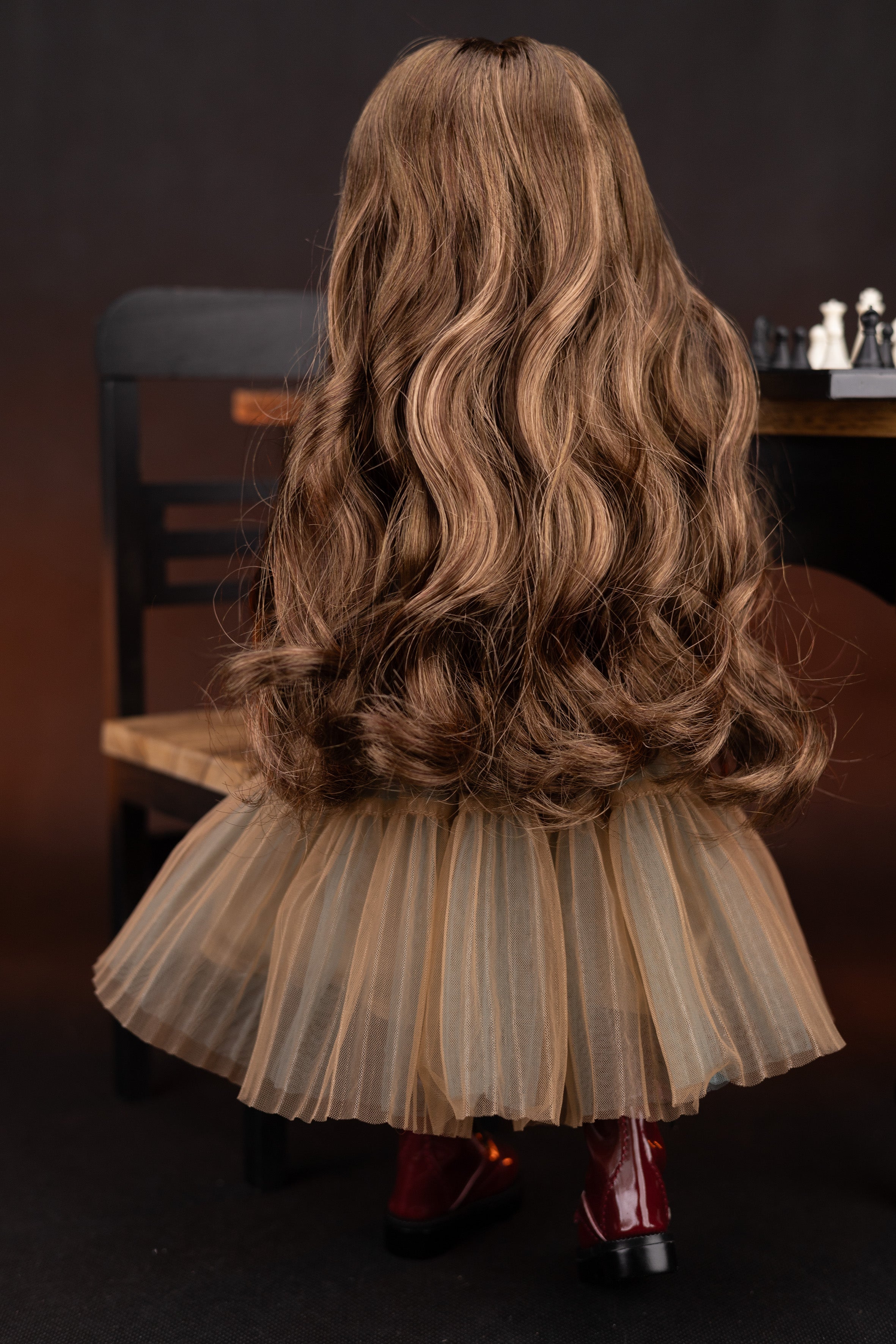 Back view of a doll with long wavy hair and a beige skirt on a dark background