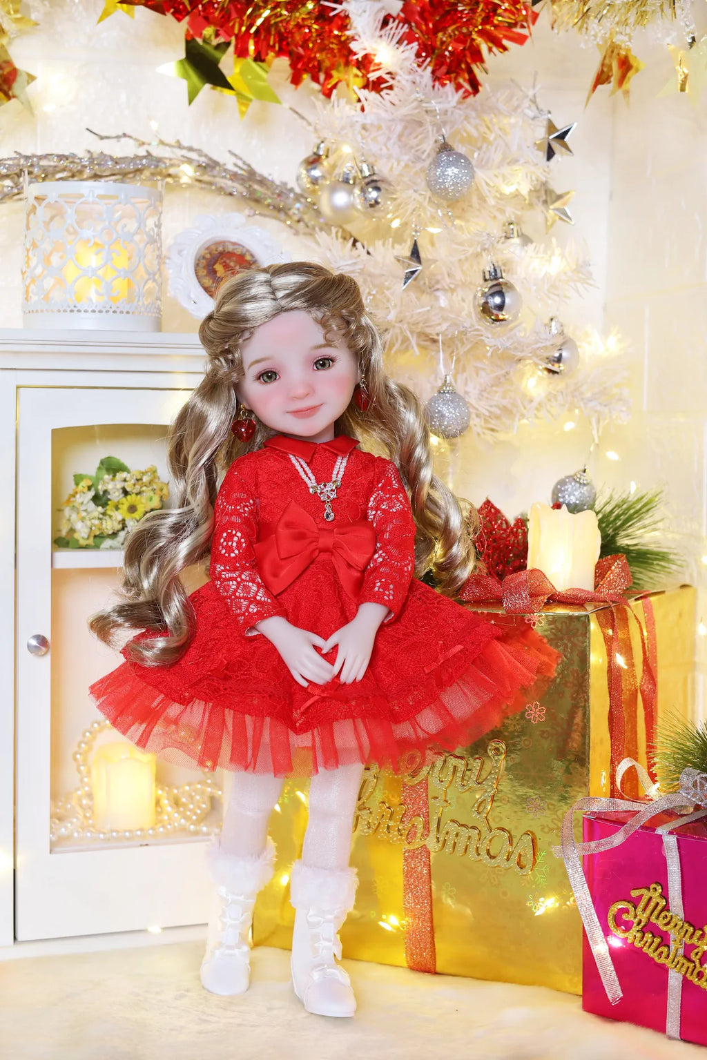 Doll in a red dress standing in front of a decorated Christmas tree with lights and presents.