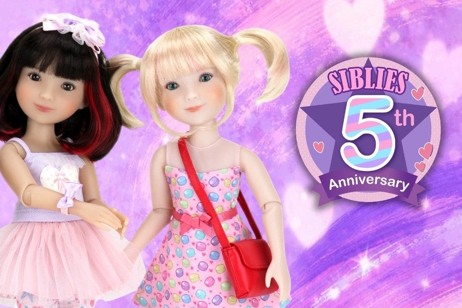 Two Siblies dolls with a 'Siblies 5th Anniversary' badge on a purple background