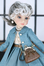 Doll wearing a dark turquoise coat with a brown handbag against a blurred background