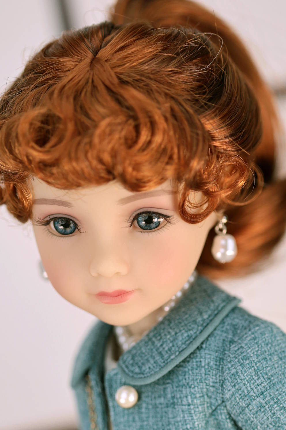 Close-up of a doll with red hair and a  dark turquoise outfit against a white background
