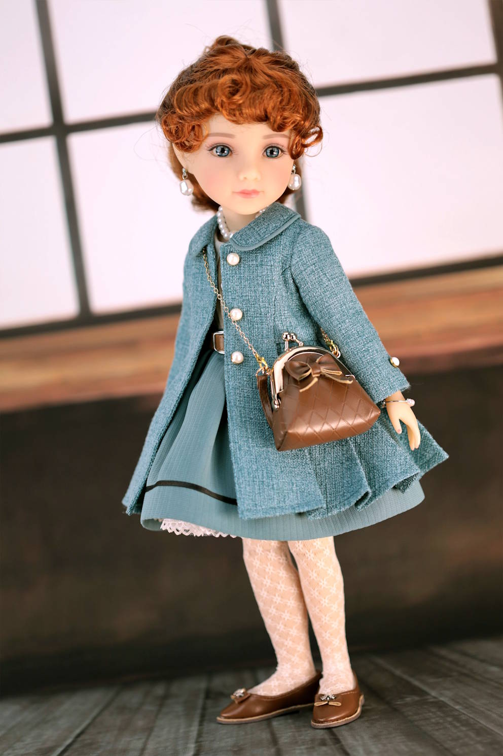 Doll wearing a dark turquoise coat and holding a brown handbag against a neutral background