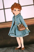 Doll wearing a dark turquoise coat and holding a brown handbag against a neutral background