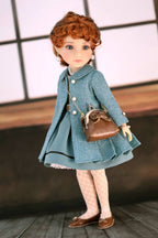 Doll wearing a dark turquoise coat and holding a brown handbag against a neutral background