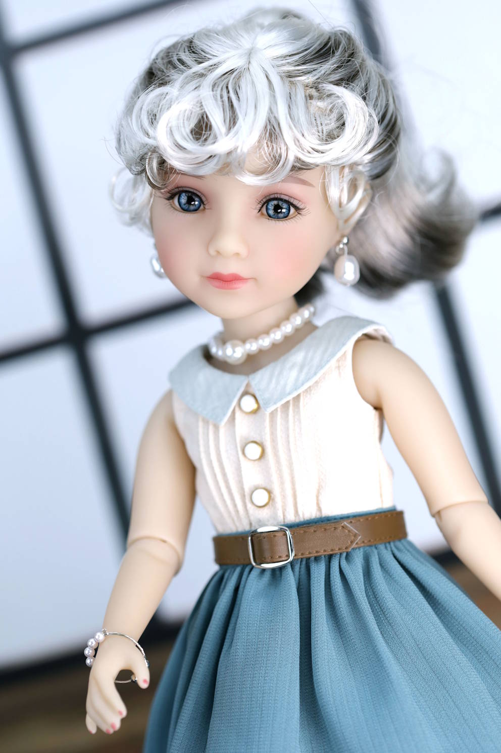 Doll with white hair, blue eyes, and a white dress with a brown belt against a blurred background