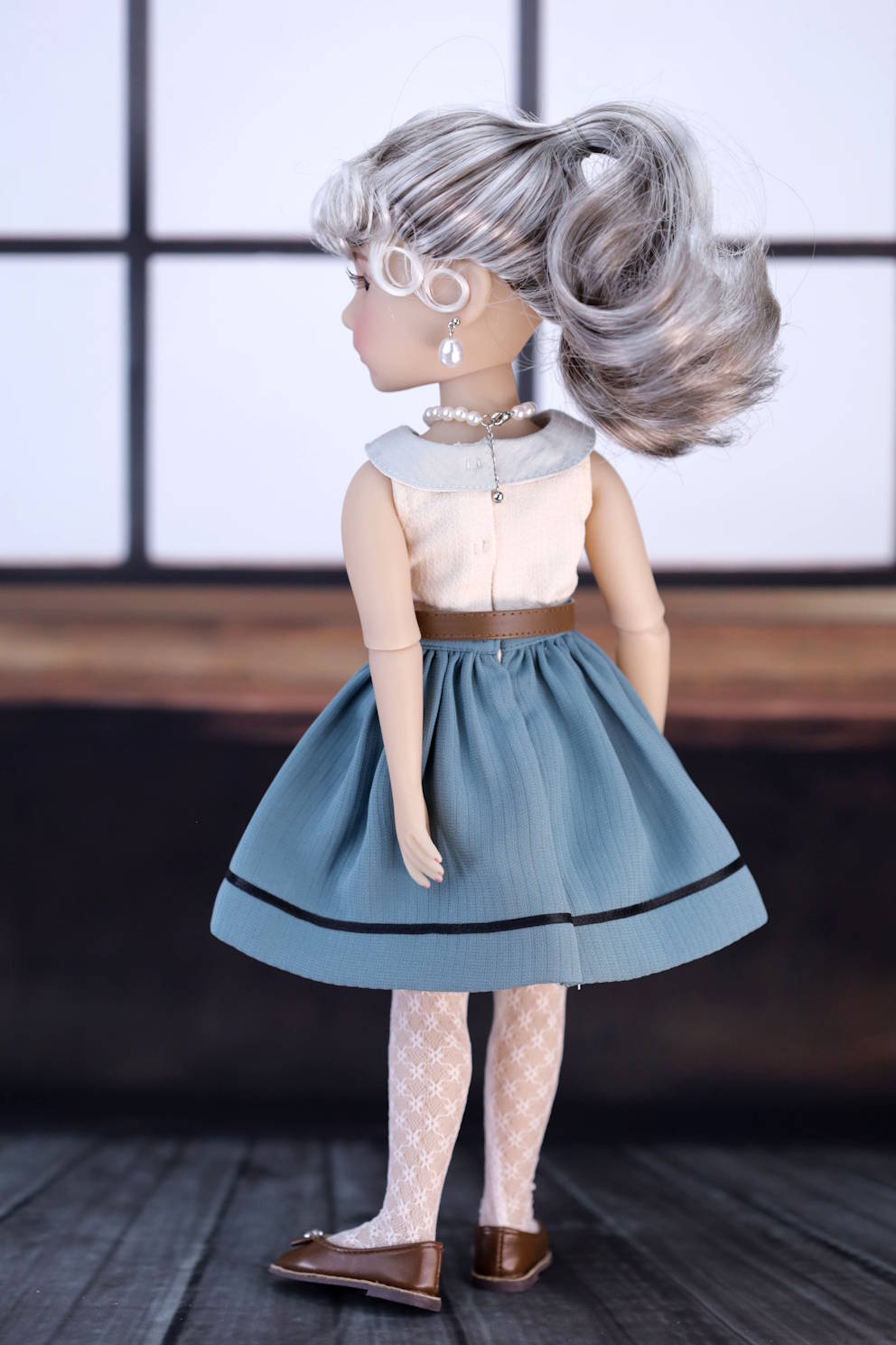 Doll with gray hair styled in an updo, wearing a light-colored top and blue skirt.