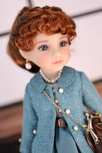 Doll with red hair wearing a dark turquoise coat and pearl necklace against a blurred background
