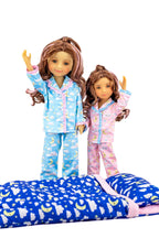 Two dolls wearing matching pajamas with a blue blanket featuring moon and star patterns.