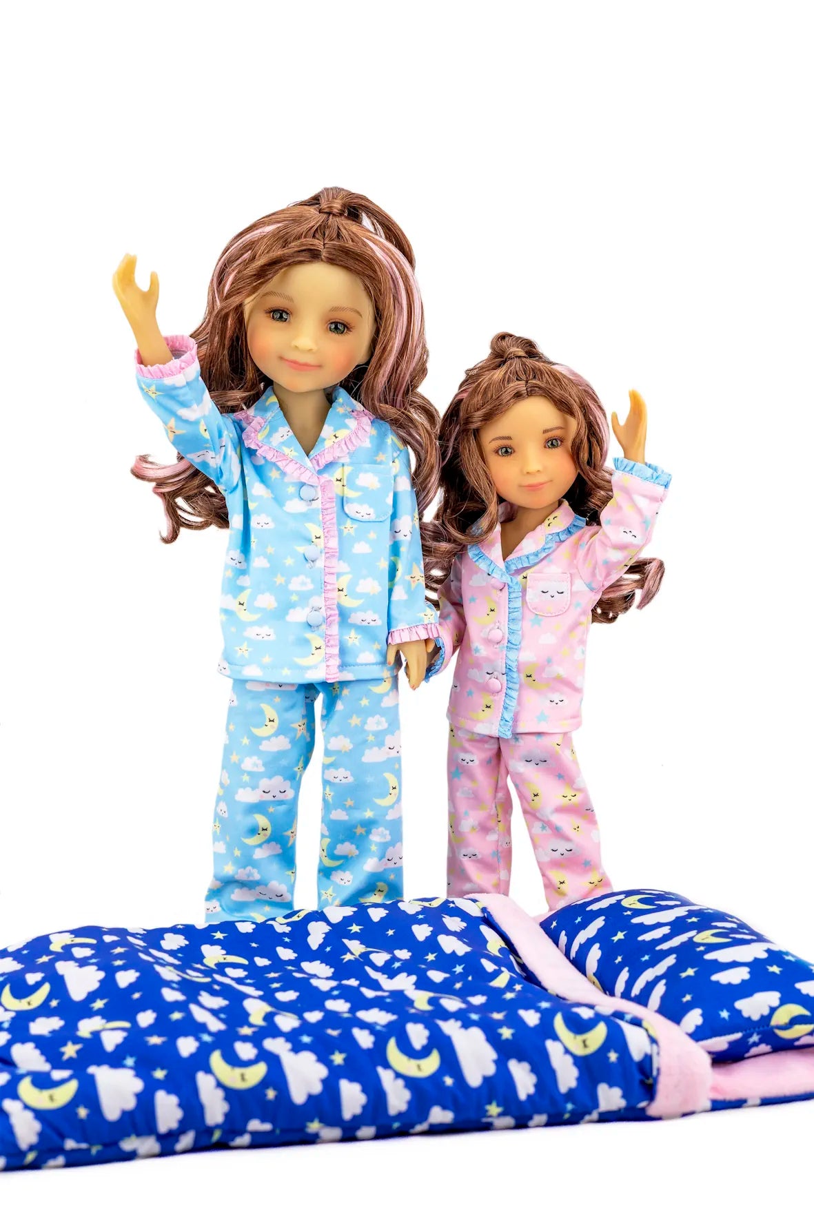 Two dolls wearing matching pajamas with a blue blanket featuring moon and star patterns.