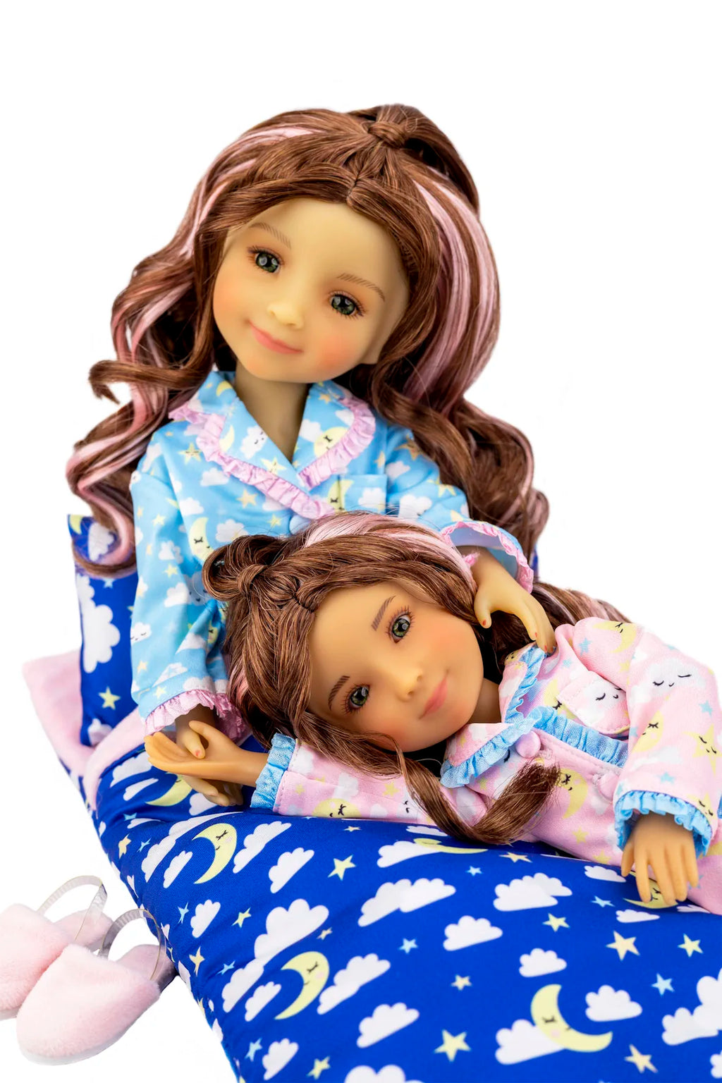 Two dolls in pajamas sitting on a blue cloud-patterned cushion.