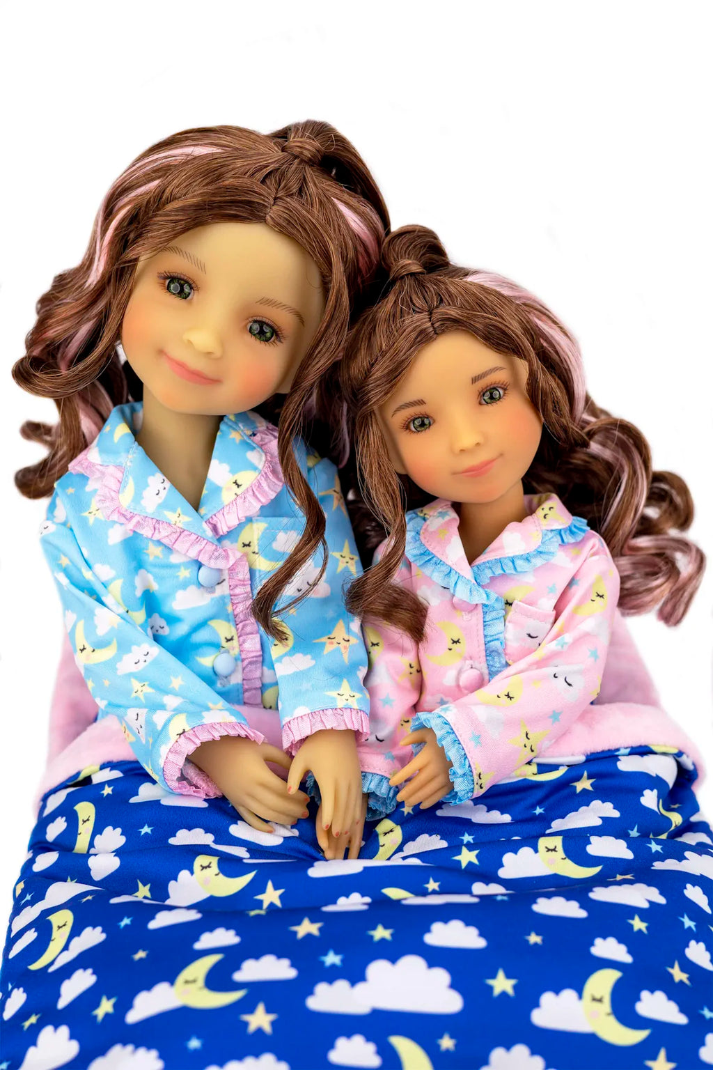 Two dolls in pajamas with a blue blanket featuring clouds and stars.
