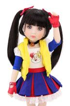 Doll with long black hair styled in pigtails, wearing a colorful outfit with a yellow vest, blue skirt, and red shoes on a white background.
