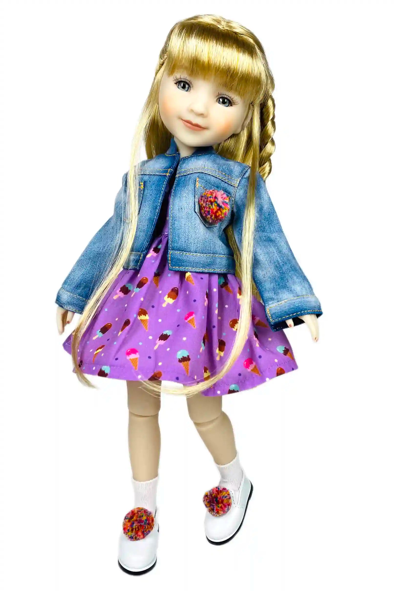 Doll wearing a denim jacket with floral pockets and a purple dress with cupcake pattern on a white background
