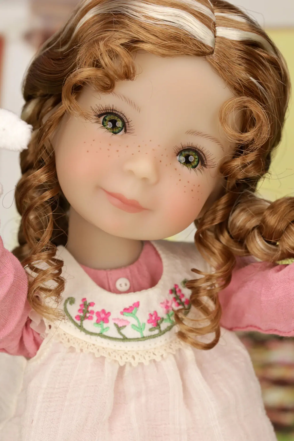 Close-up of a doll with braided hair wearing a pink dress with floral embroidery.