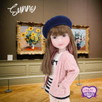 Doll named Sunny in a pink sweater and blue beret standing in front of art pieces