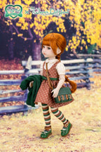 Doll in a brown polka dot dress with suspenders standing in a scenic outdoor setting.