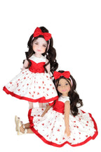 Two dolls in matching red and white dresses with heart patterns on a white background
