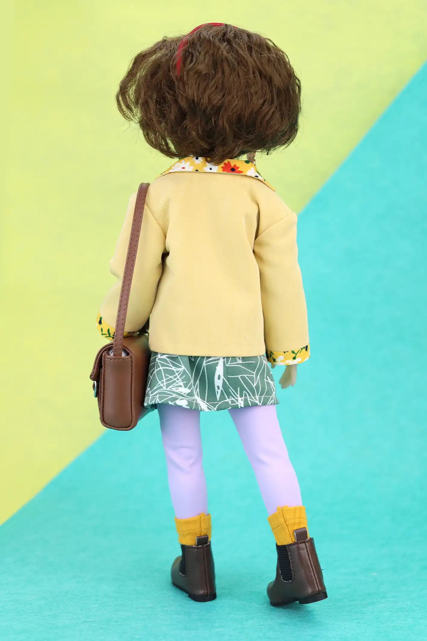 Ava wearing a yellow coat and colorful outfit on a green and blue geometric background