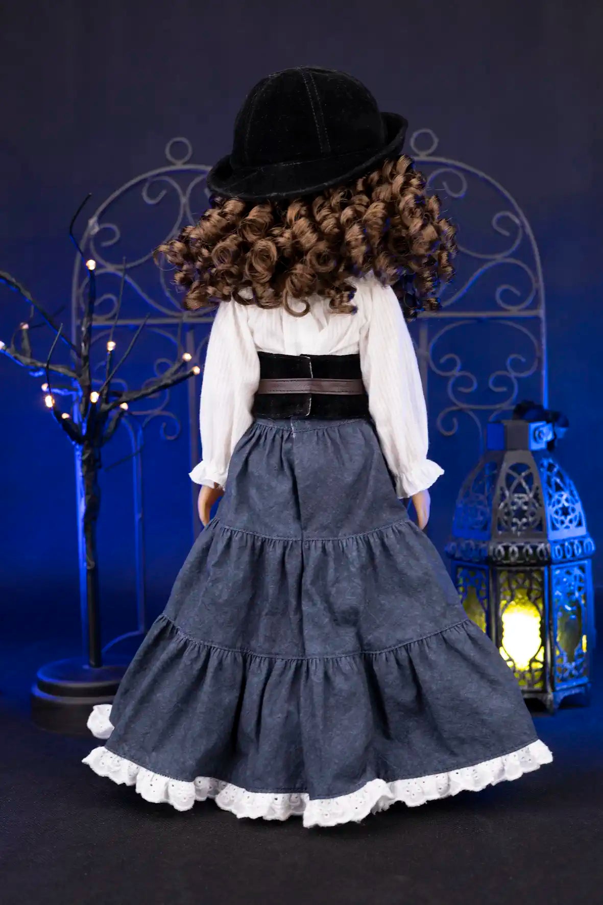 Clark wearing a long dark blue dress with white trim and a black hat, standing in front of decorative lights and a metal arch.