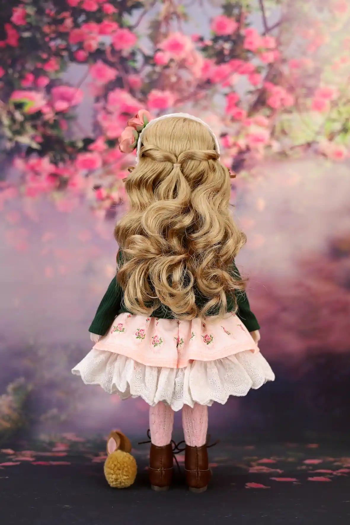 Eden with long blonde hair and a green dress standing in front of cherry blossoms.