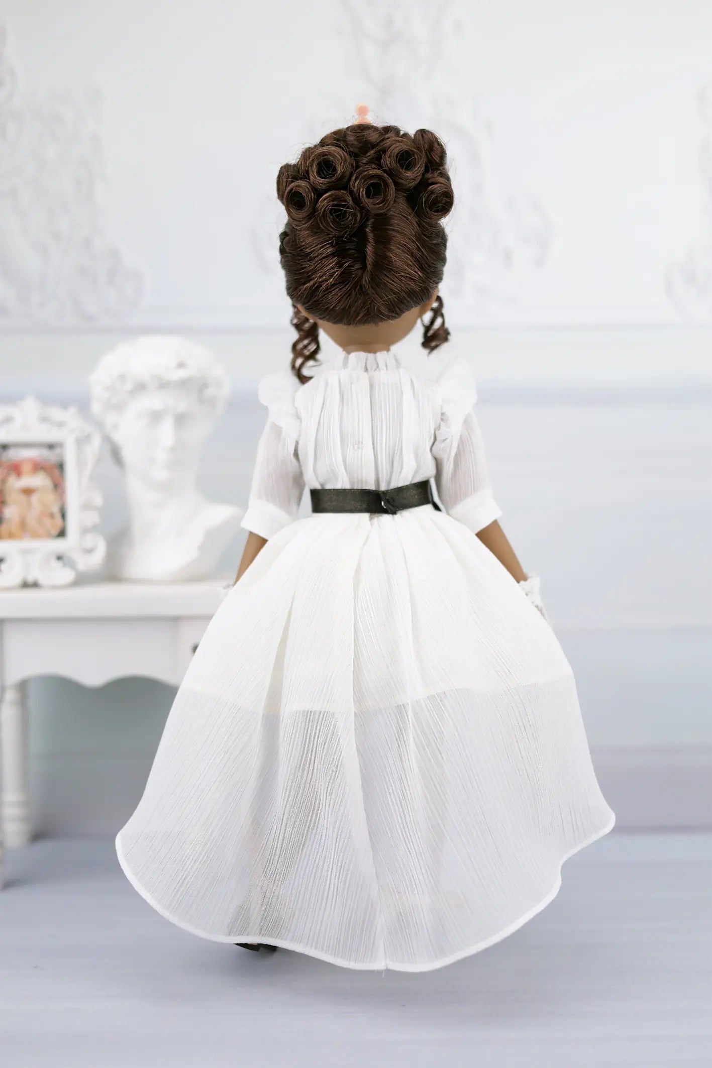 Esther in a white dress with a black belt against a light gray background