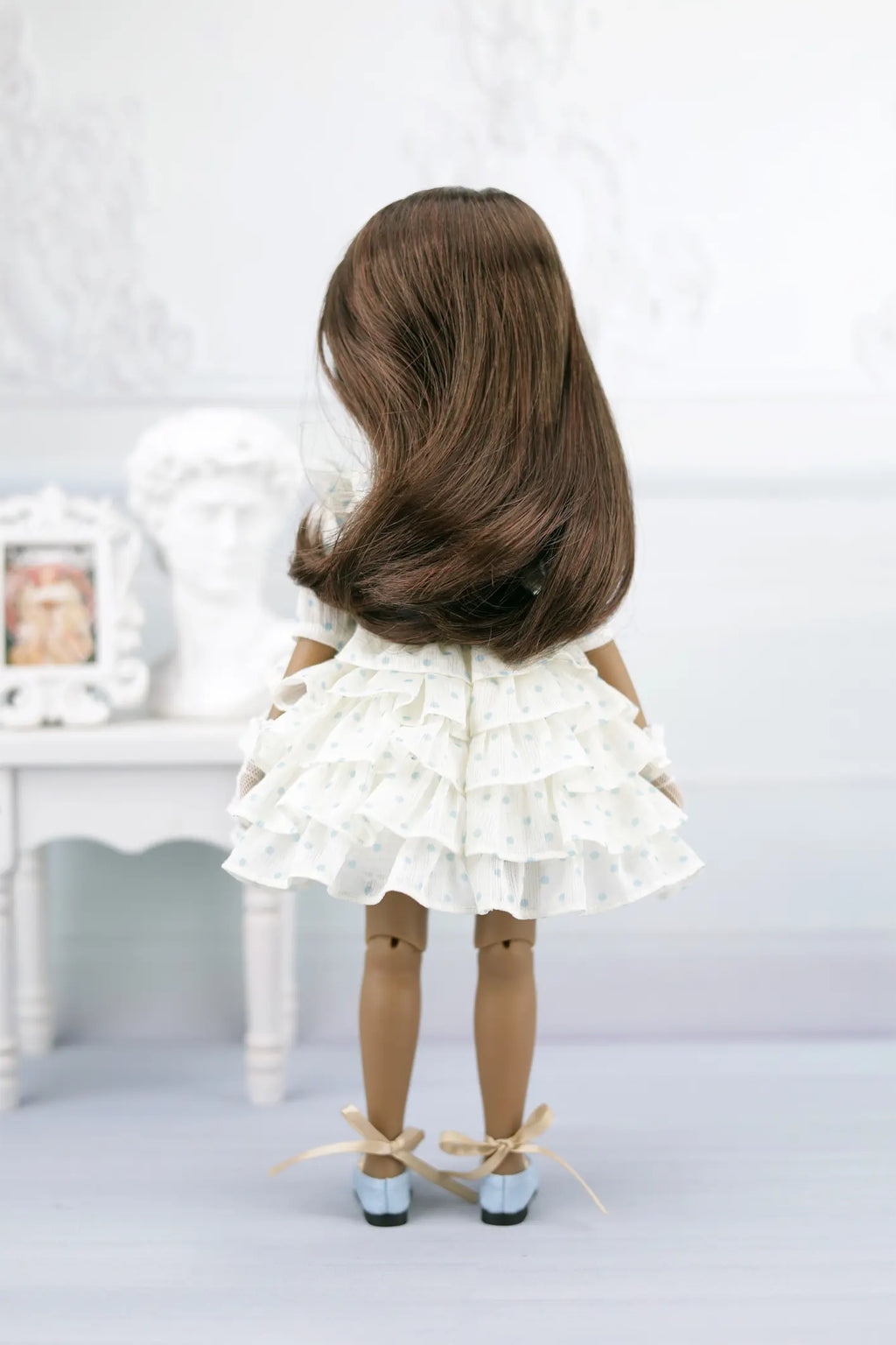 Ruth with long brown hair wearing a white dress and shoes on a light background