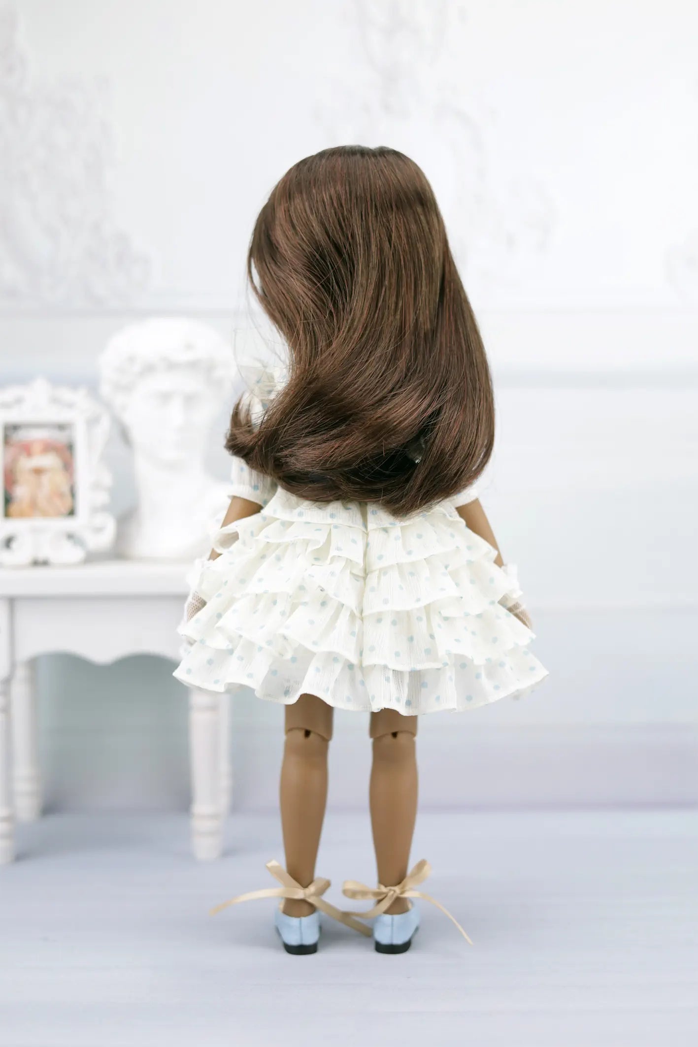 Ruth with long brown hair wearing a white dress and shoes on a light background