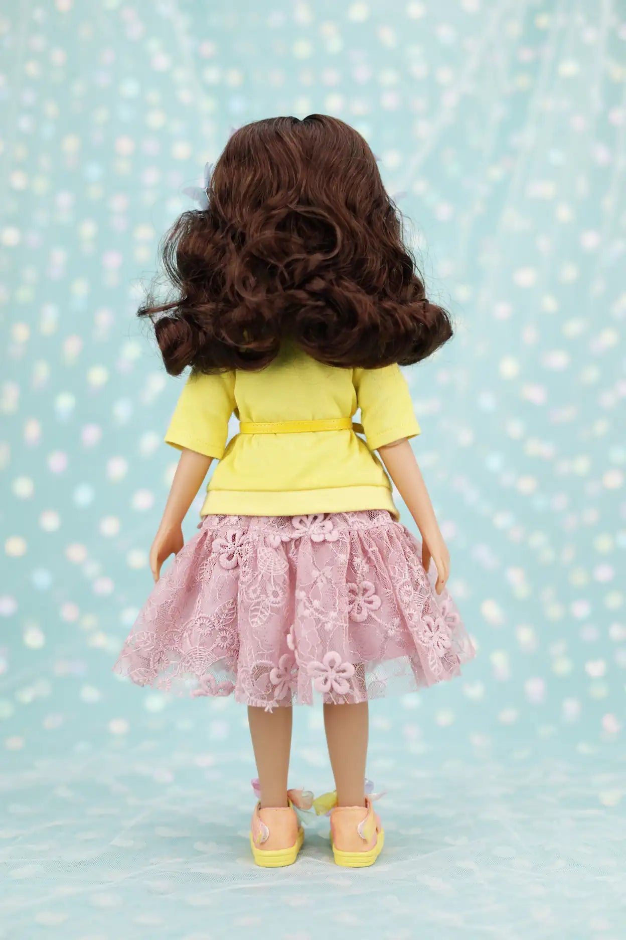 Juniper wearing a yellow top and pink skirt with floral details on a light blue background