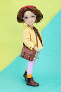 Ava wearing a yellow jacket and brown shoes on a green and blue background