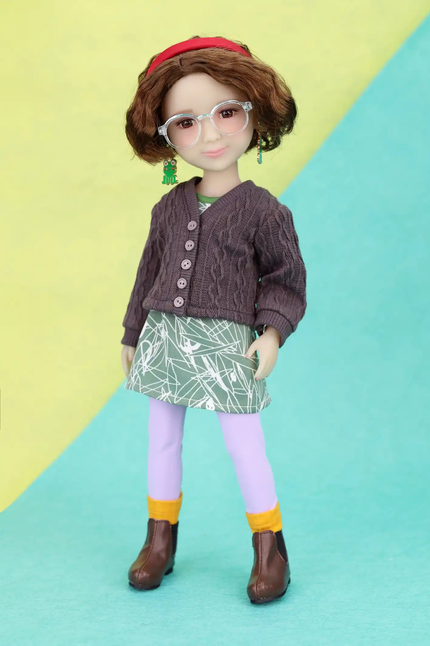 Ava wearing a brown cardigan, green skirt, and purple leggings on a yellow and blue background