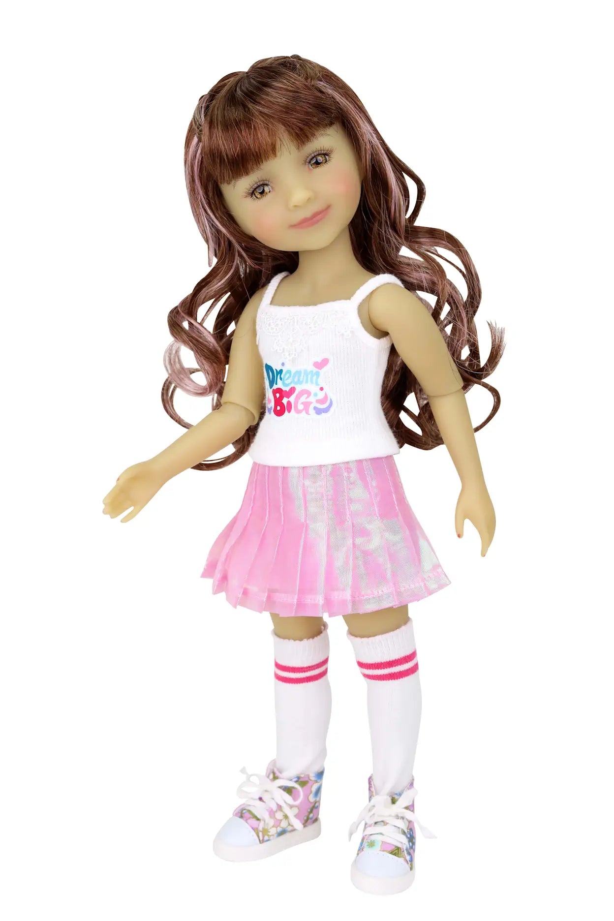 Bella with long wavy brown hair, wearing a white 'Dream Big' tank top, pink skirt, white socks with pink stripes, and floral sneakers, white background.