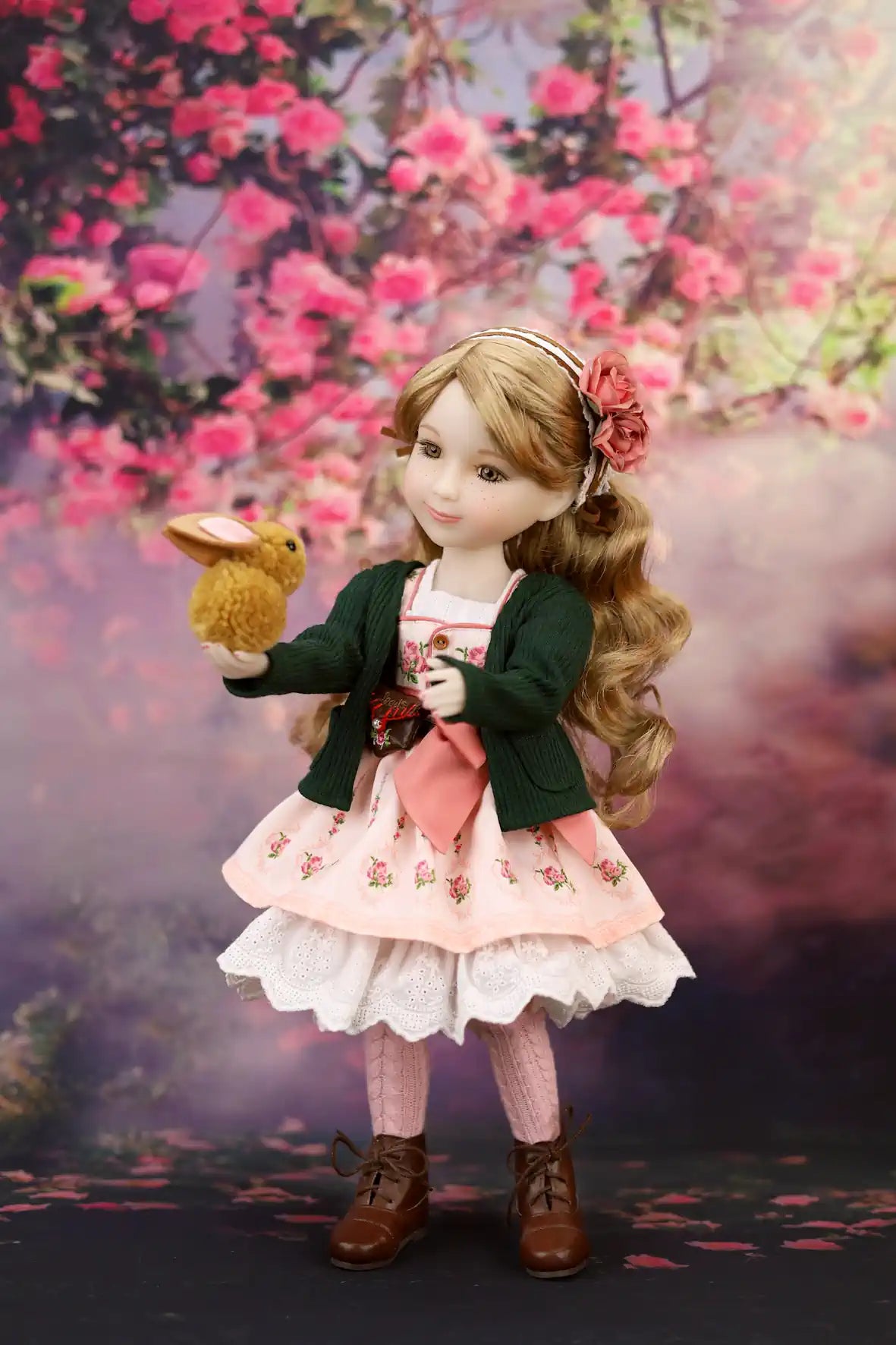 Eden in a pink dress with a green jacket holding a rabbit toy, standing against a floral background.