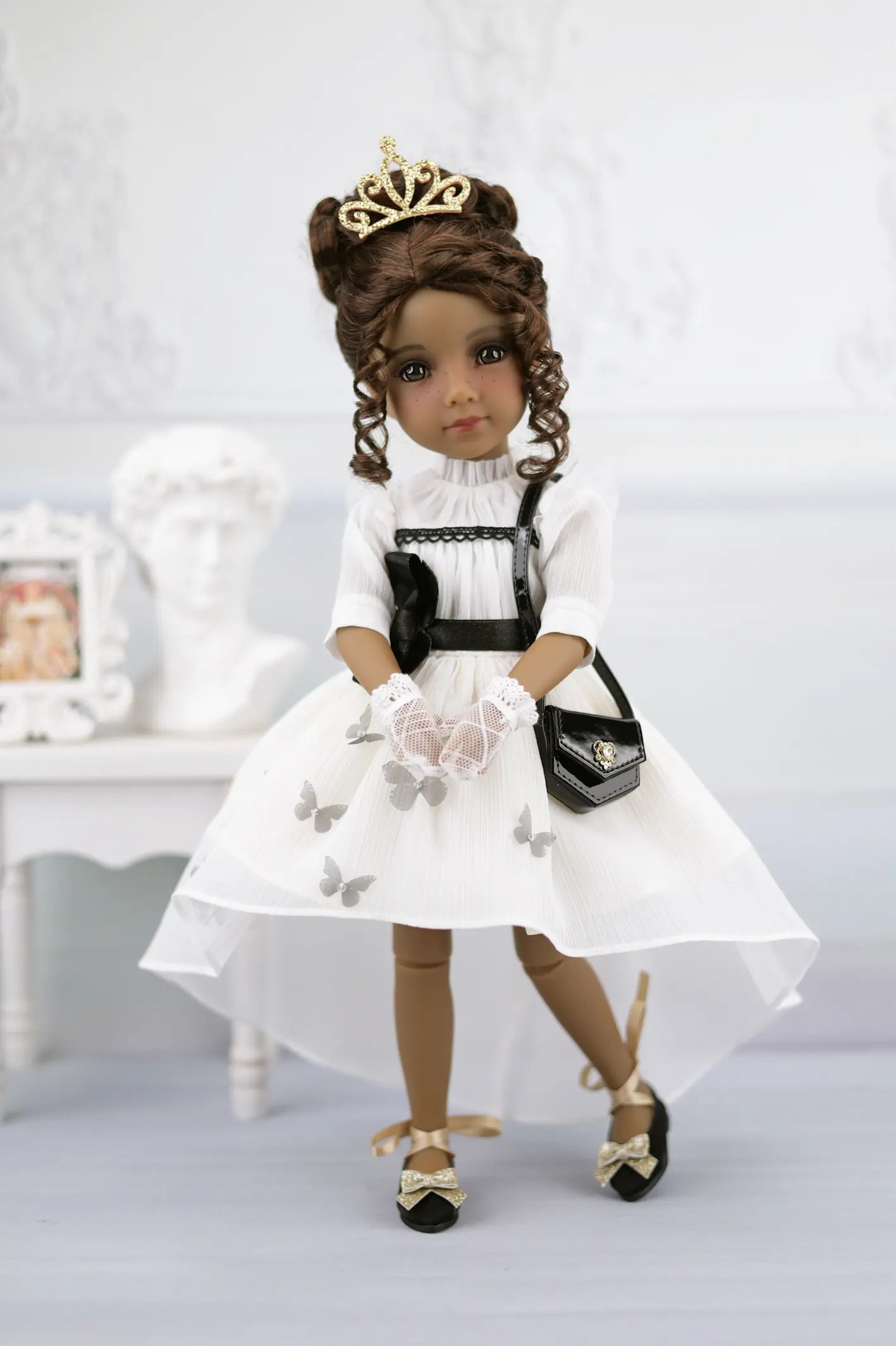 Esther in a white dress with a black handbag and tiara on a light background