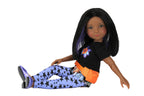 Kelsey wearing a black shirt with a colorful design, blue pants with star pattern, and orange belt on a white background