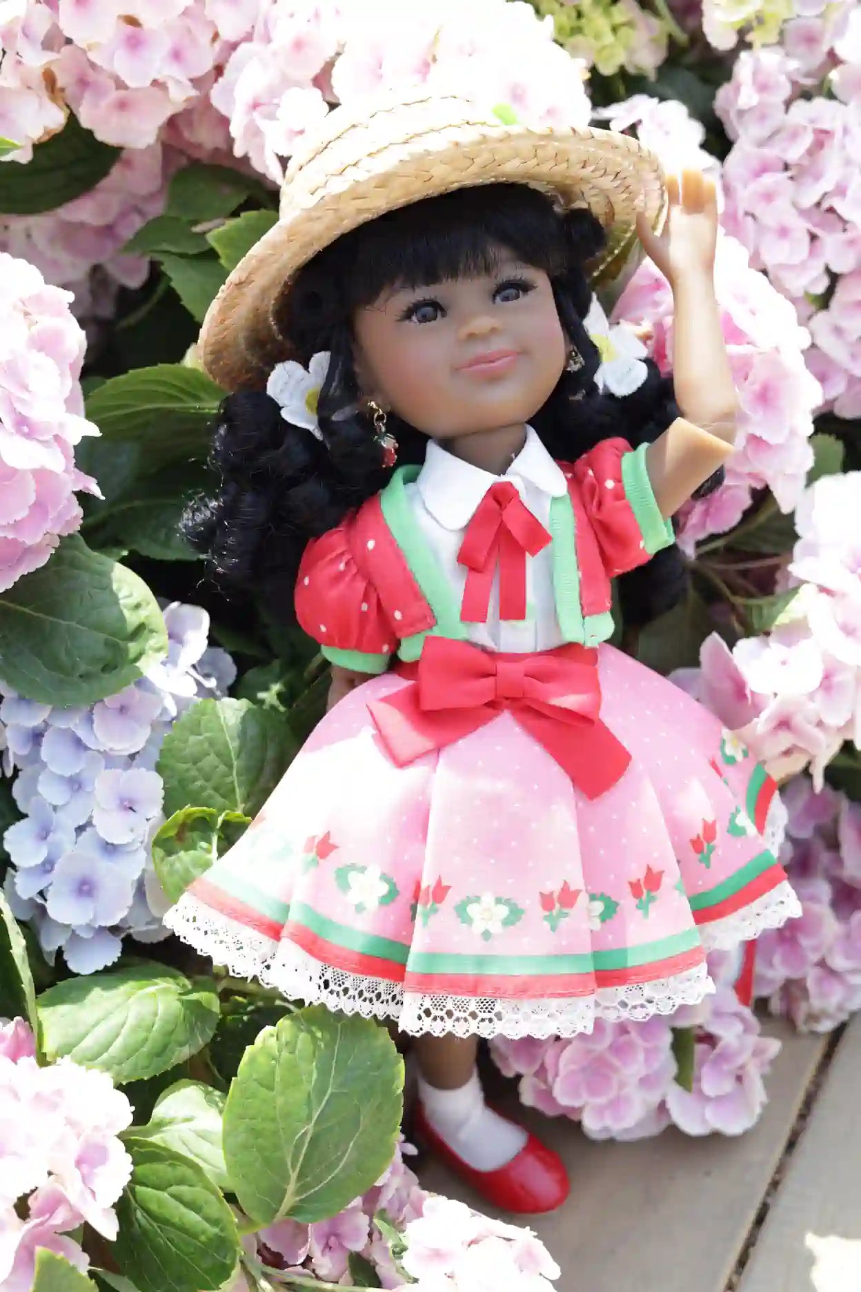 Kyra in a pink dress with a straw hat surrounded by pink flowers