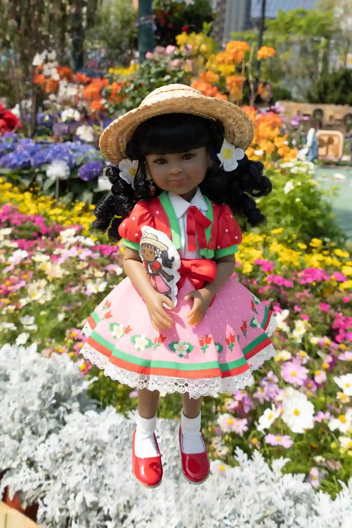 Kyra in a strawberry-themed outfit with a hat, standing in a garden with flowers.