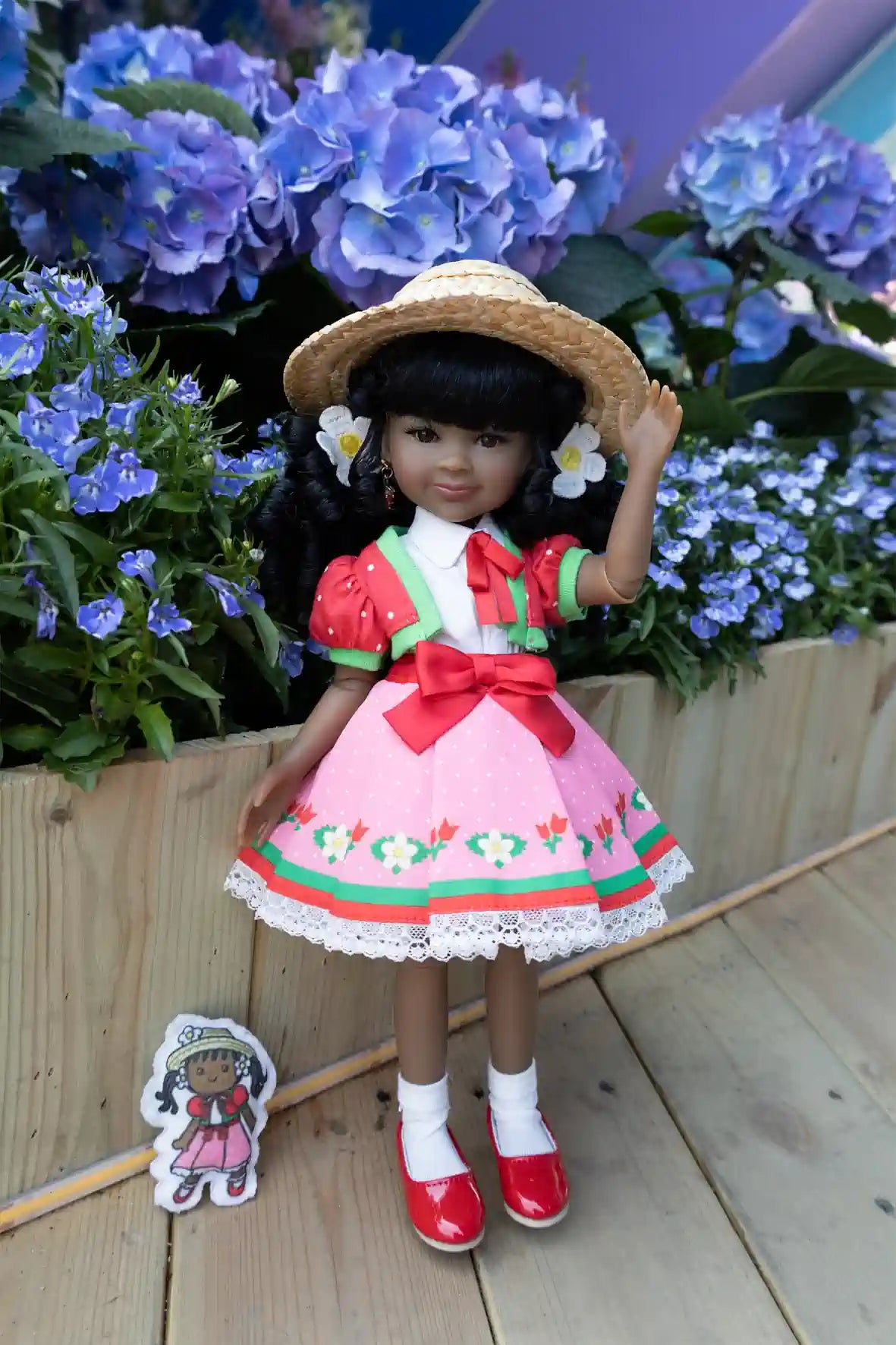 Kyra in a pink dress with a straw hat standing in front of blue flowers