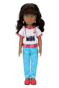 Mila, a doll with curly dark brown hair, wears a white t-shirt with a camera graphic, light blue pants, red shoes,  against a white background.