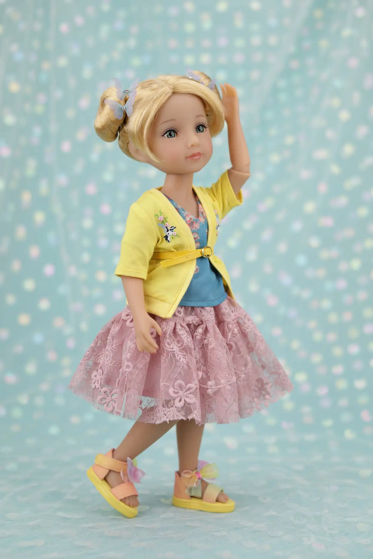Juniper wearing a yellow cardigan, blue top, and pink skirt against a light blue background with polka dots.