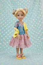 Juniper with blonde hair styled in buns, wearing a yellow cardigan over a blue shirt and pink skirt, on a light blue background with polka dots.