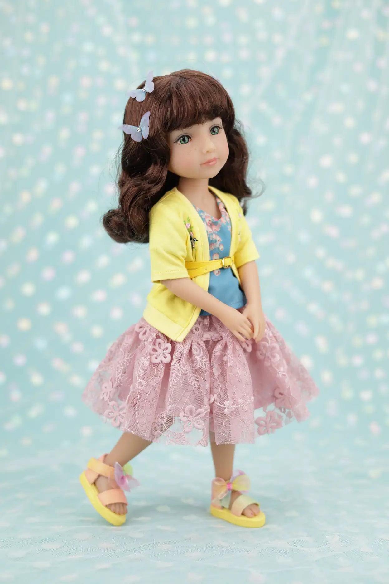 Juniper wearing a yellow cardigan, pink dress, and sandals on a light blue background