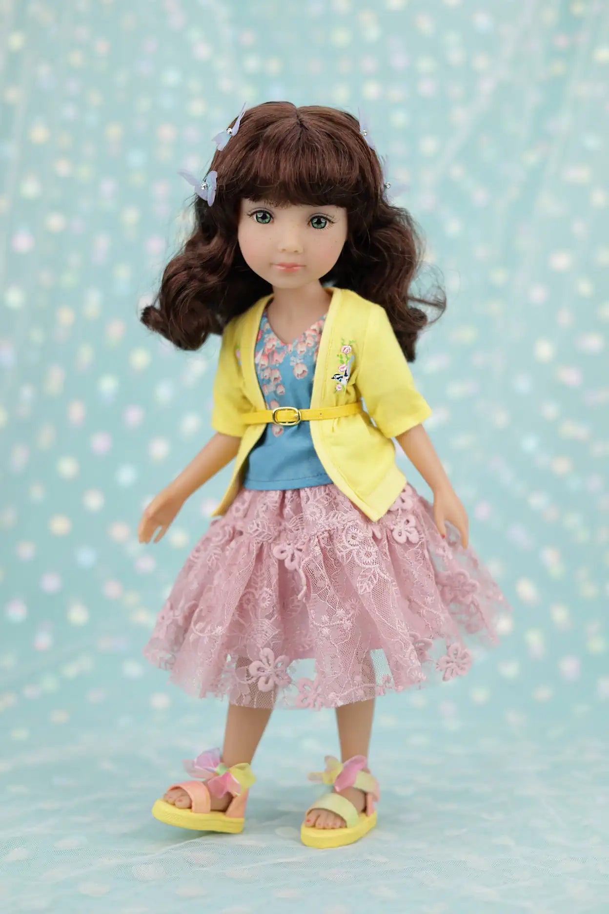 Juniper wearing a yellow jacket, blue shirt, and pink dress with a floral pattern on a light blue background.