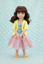 Juniper wearing a yellow cardigan, pink dress, and sandals on a light blue polka dot background