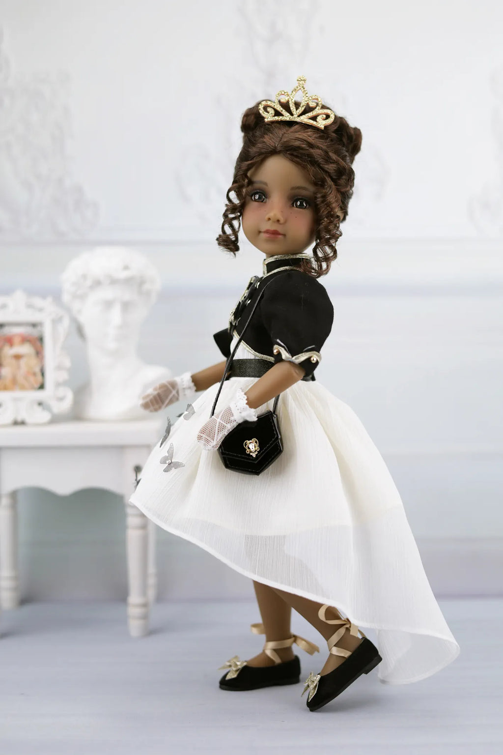 Esther in formal attire with a white dress, black jacket, and gold tiara on a light background.