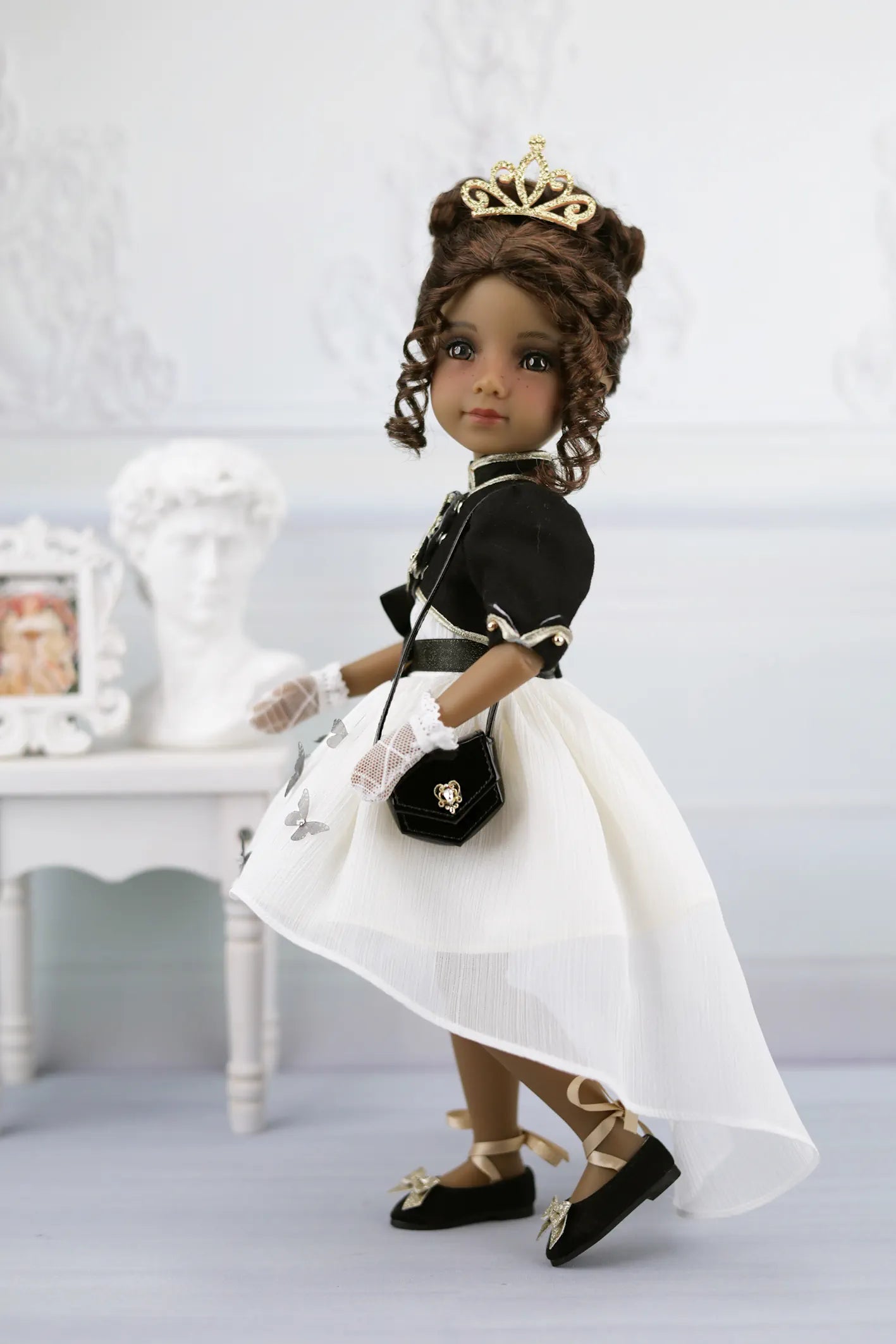 Esther in formal attire with a white dress, black jacket, and gold tiara on a light background.
