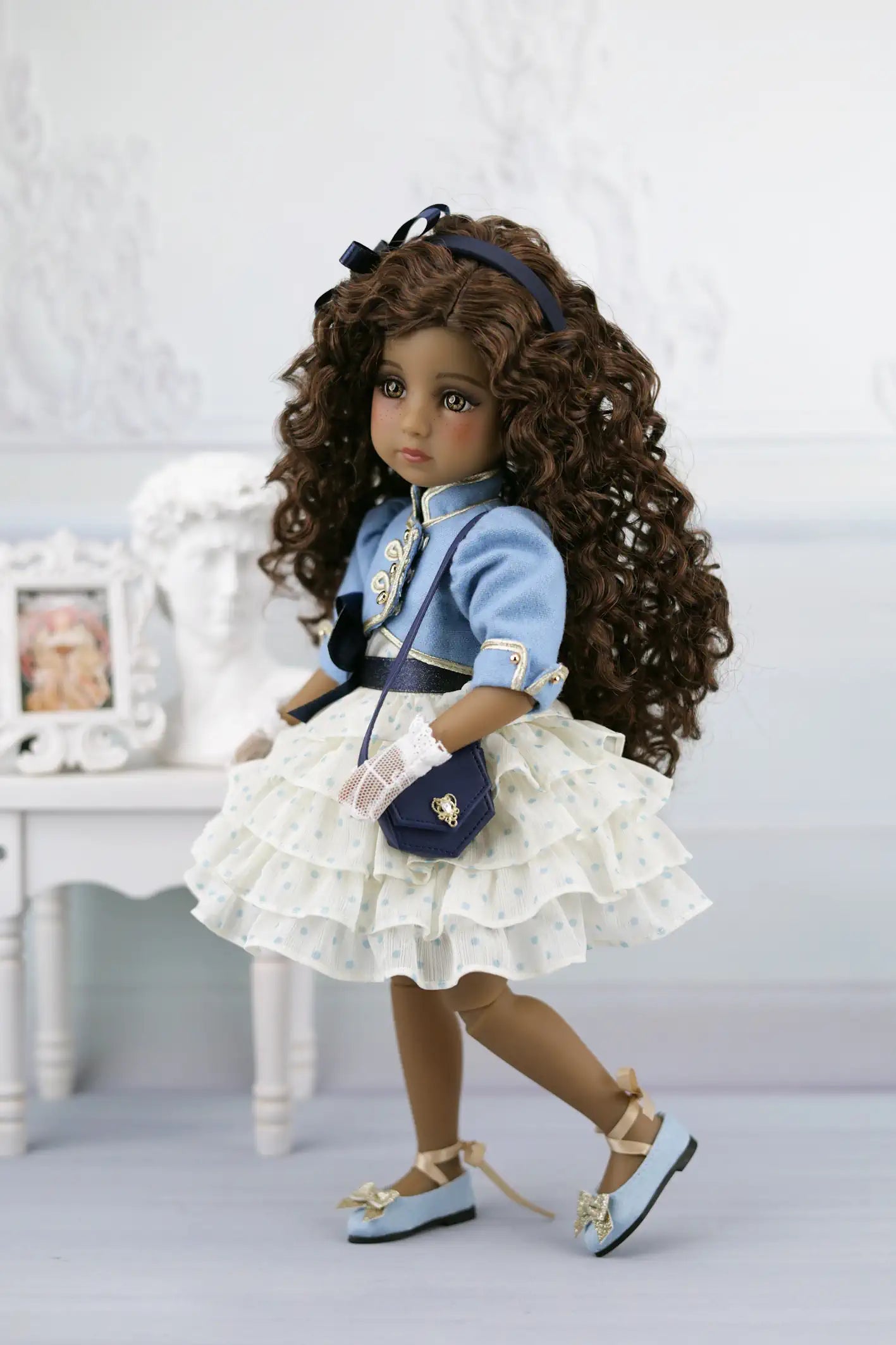 Ruth with curly hair wearing a blue outfit with a white ruffled skirt in a decorative setting.