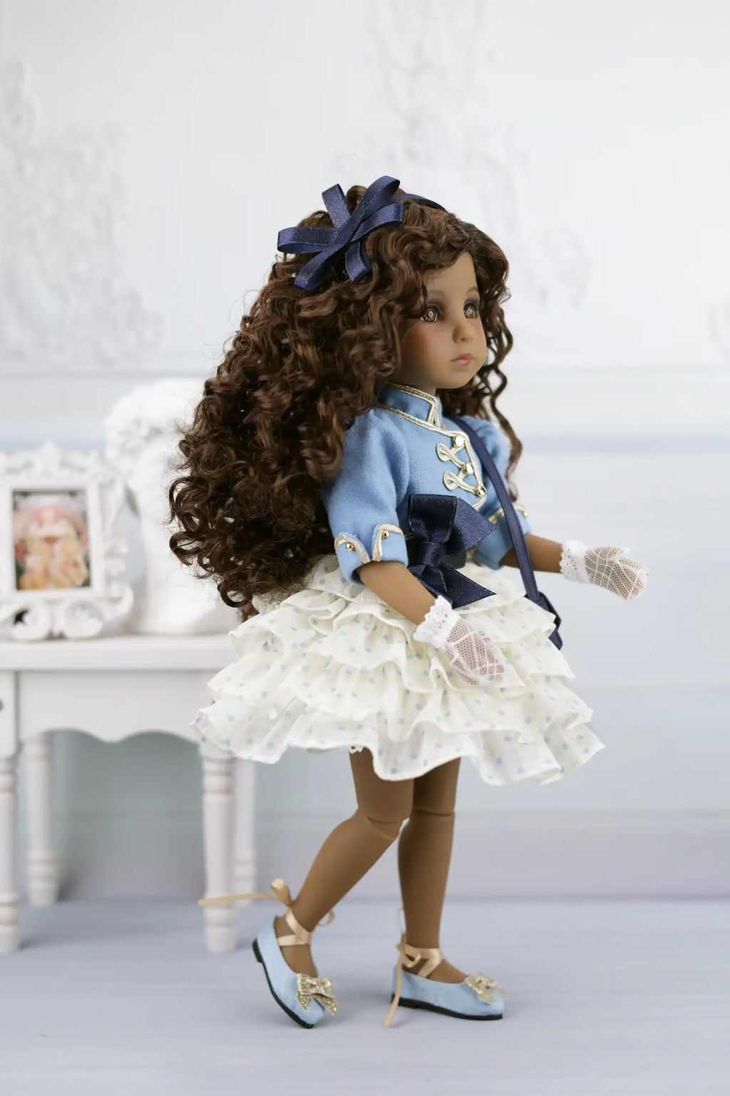 Ruth with long curly hair wearing a blue dress and white shoes on a light background