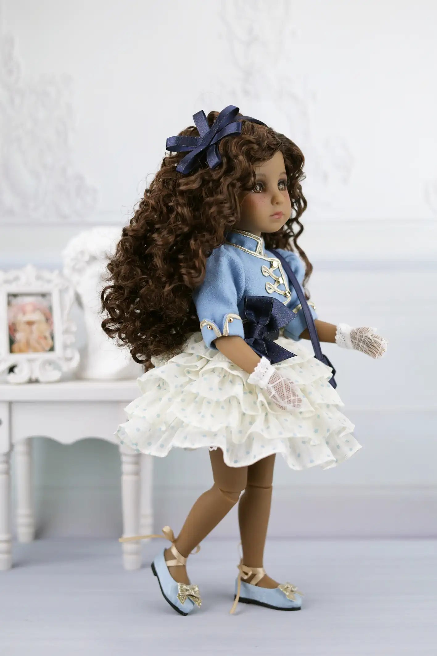 Ruth with long curly hair wearing a blue dress and white shoes on a light background